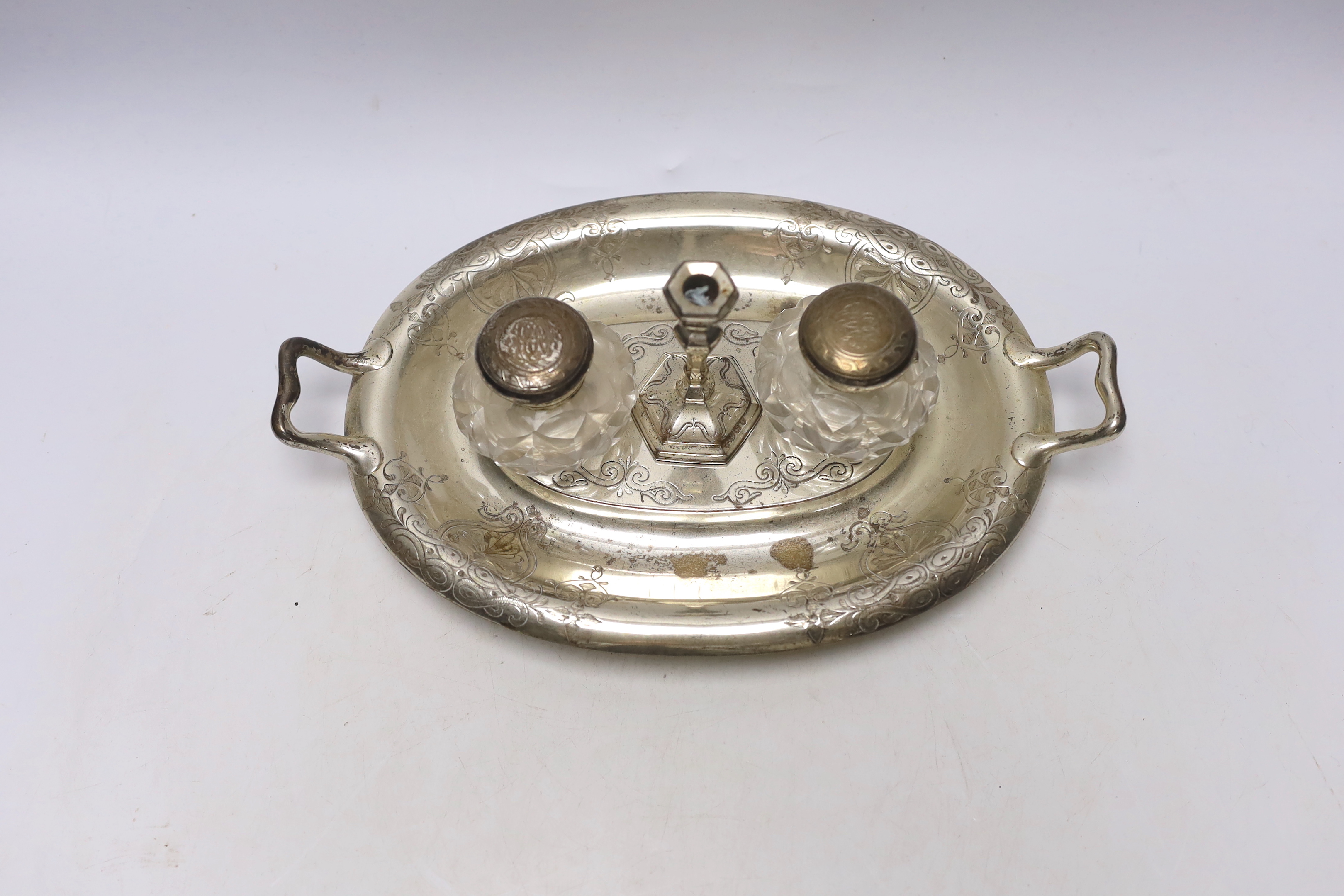 A Victorian engraved silver oval two handled inkstand, with two mounted glass wells and a taperstick, on four scroll feet, Henry Wilkinson & Co Ltd, 1858, 30.4cm over handles, 15.6oz.